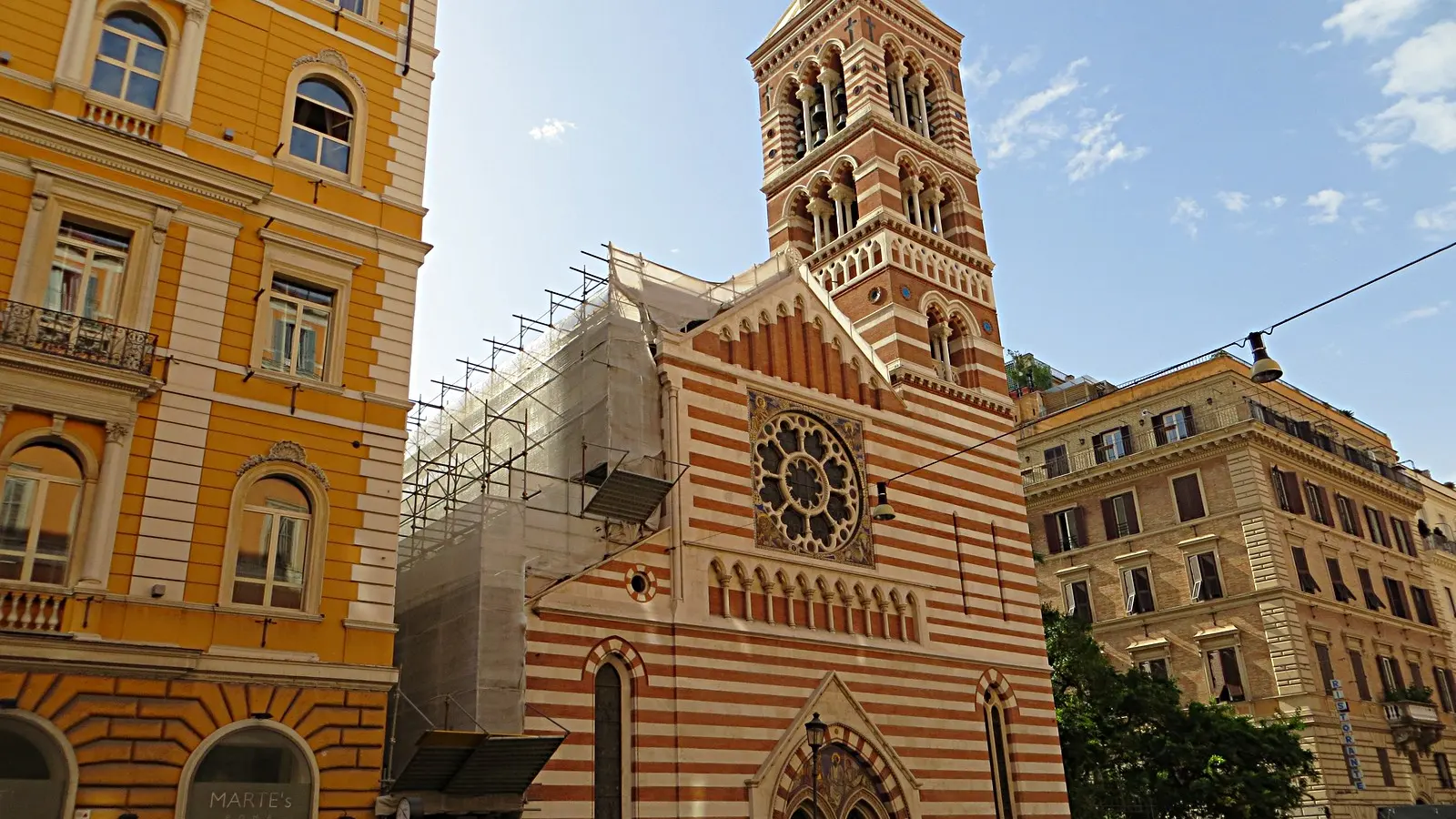 The striped red brick and pale stone Gothic Revival facade and bell tower of St Paul's Within the Walls church on Via Nazionale in Rome at 19:30 on a clear evening, st paul's within the walls